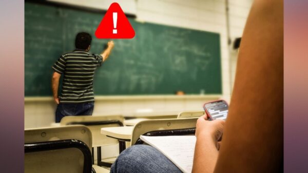 Teacher writing on a chalkboard with a warning sign next to their head