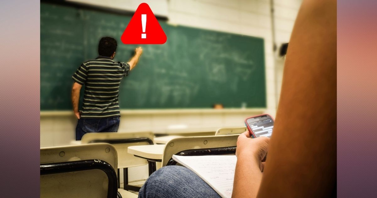 Teacher writing on a chalkboard with a warning sign next to their head